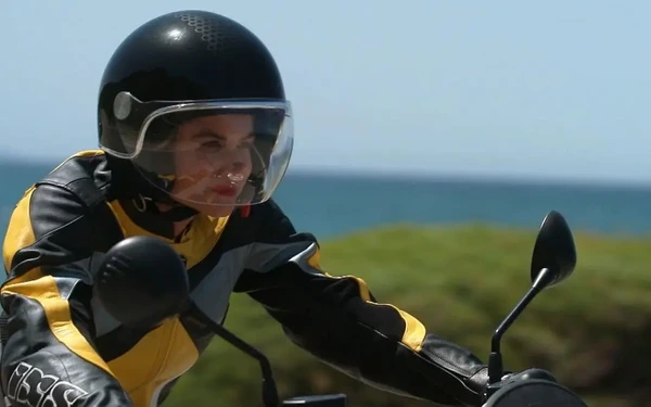 A woman rides a motorcycle, wearing a helmet in Princess Charming Season 2.
